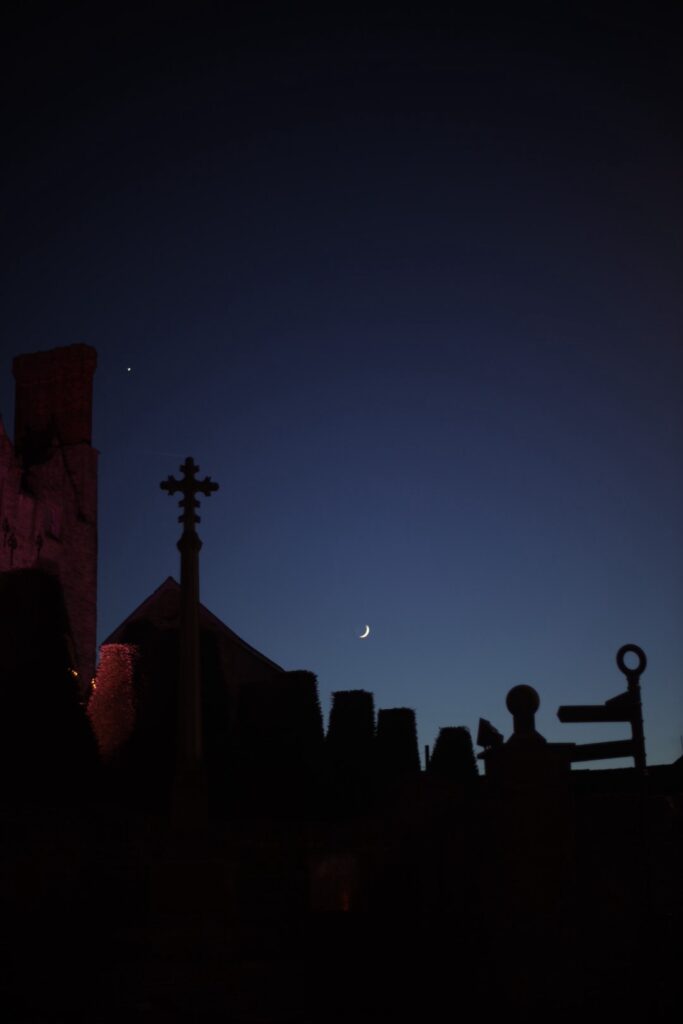 new moon and Venus at dusk, over a medieval church in Wales